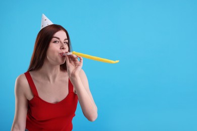 Photo of Young woman in party hat with blower on light blue background, space for text