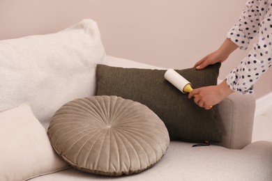 Young woman cleaning pillow with lint roller on sofa, closeup