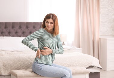 Photo of Young woman suffering from back pain at home