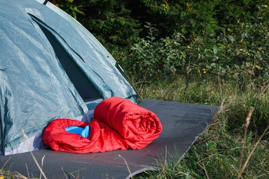 Photo of Red sleeping bag near camping tent on green grass outdoors, space for text
