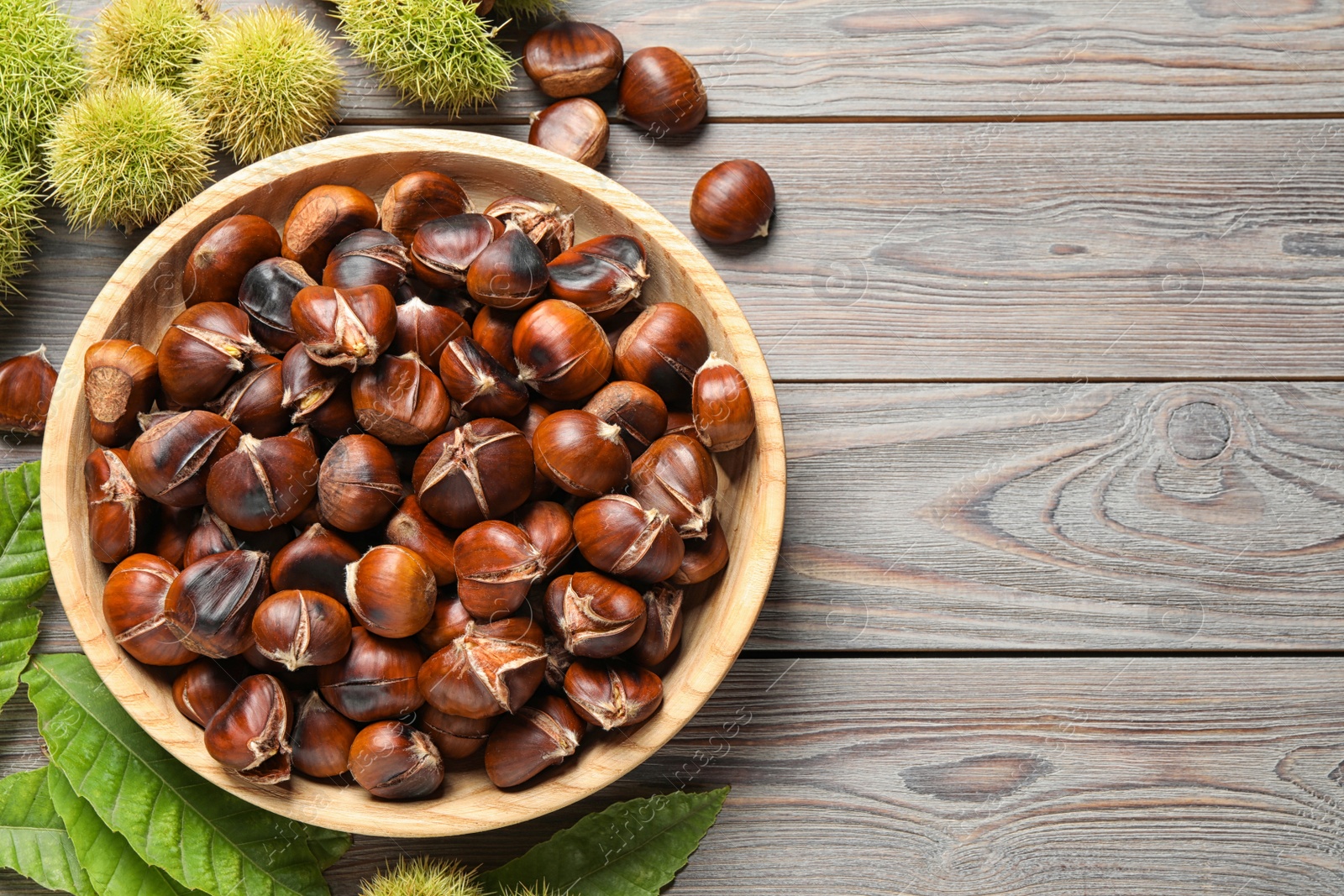 Photo of Delicious roasted edible chestnuts on brown wooden table, flat lay. Space for text