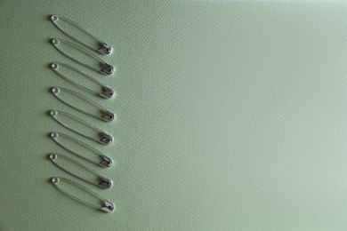 Many safety pins on green background, flat lay. Space for text