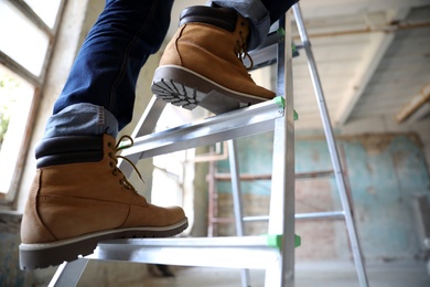 Photo of Professional constructor on ladder in old building, closeup