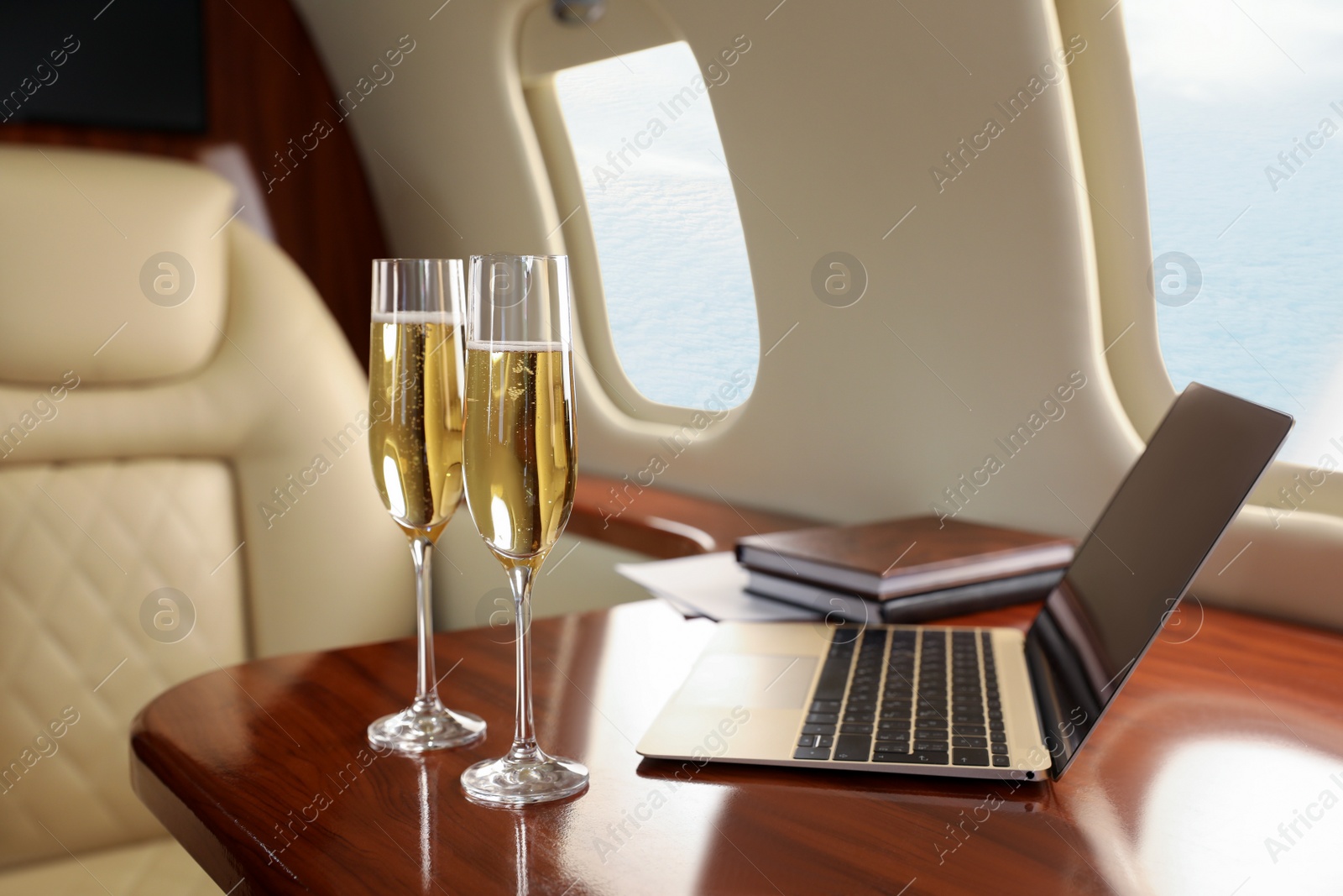 Photo of Glasses of champagne with laptop and notebooks on table in airplane