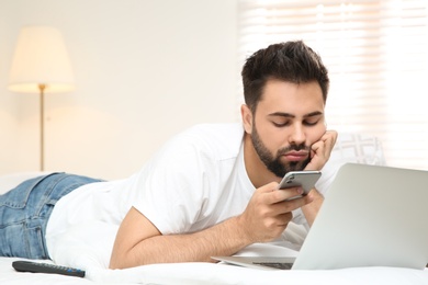 Lazy young man with laptop and smartphone on bed at home