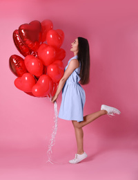 Beautiful young woman with heart shaped balloons on pink background. Valentine's day celebration