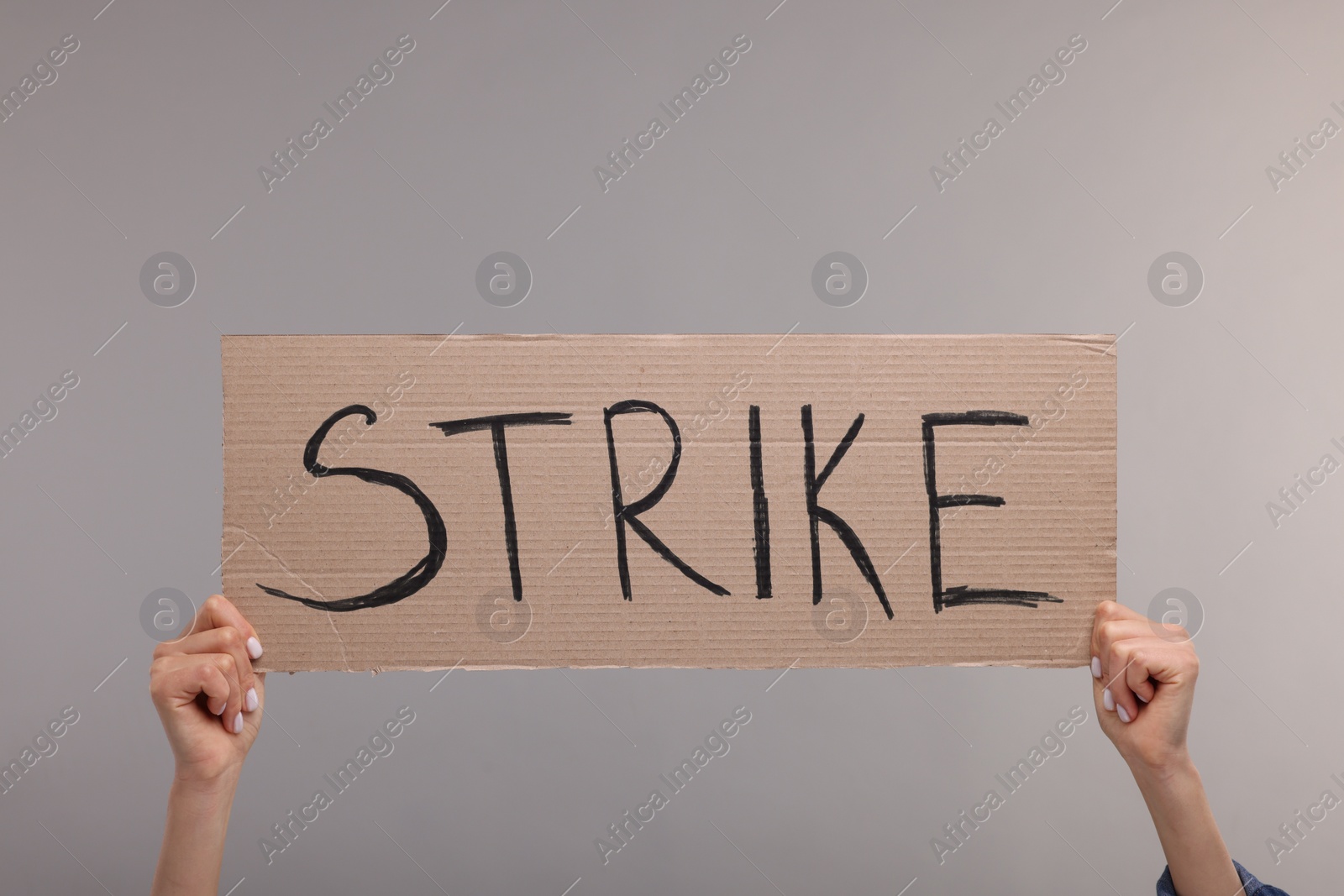 Photo of Woman holding cardboard banner with word Strike on grey background, closeup