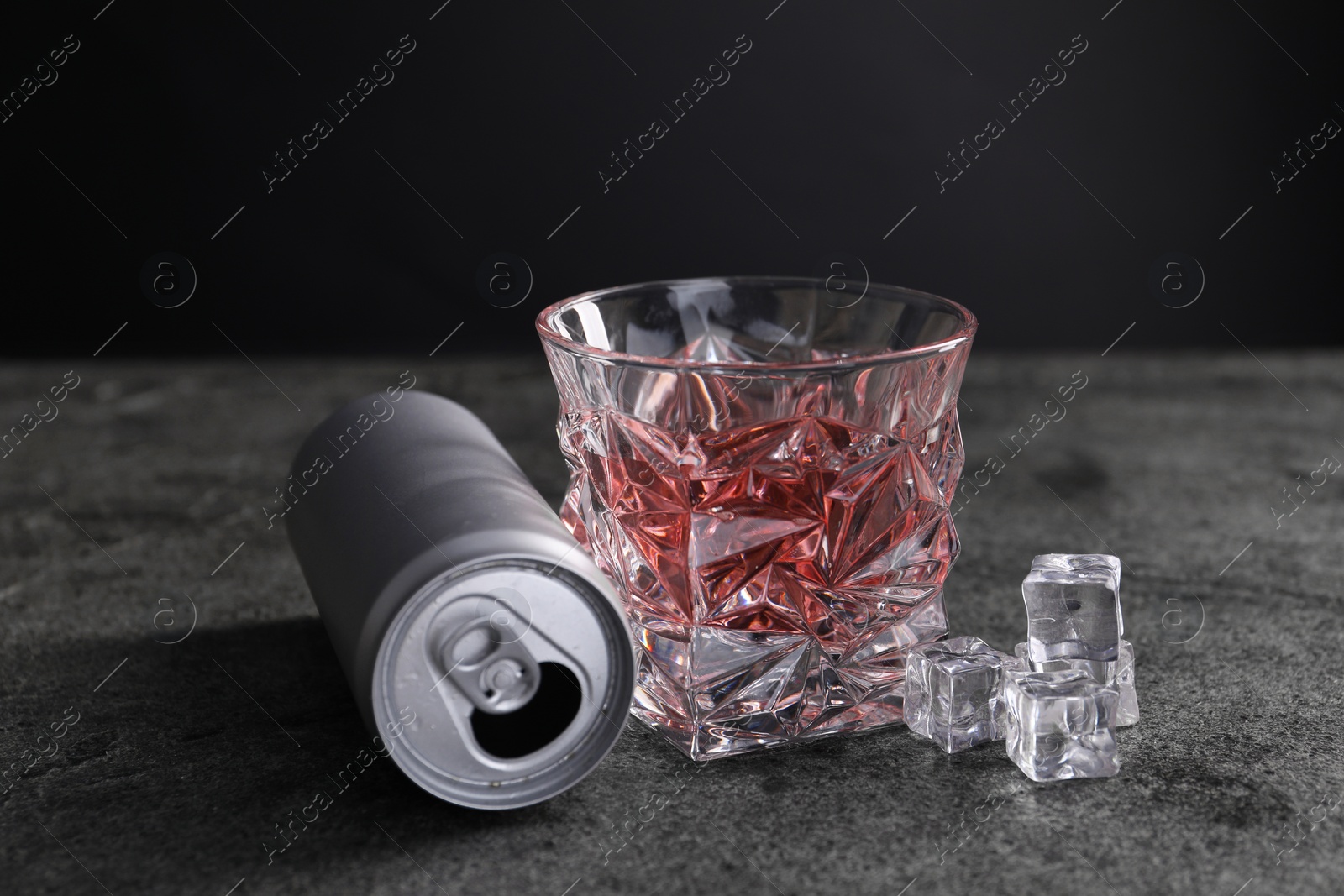 Photo of Energy drink in glass, aluminium can and ice cubes on grey table