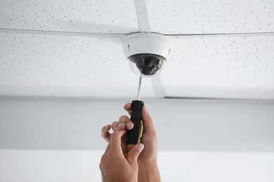 Photo of Technician installing CCTV camera on ceiling indoors, closeup