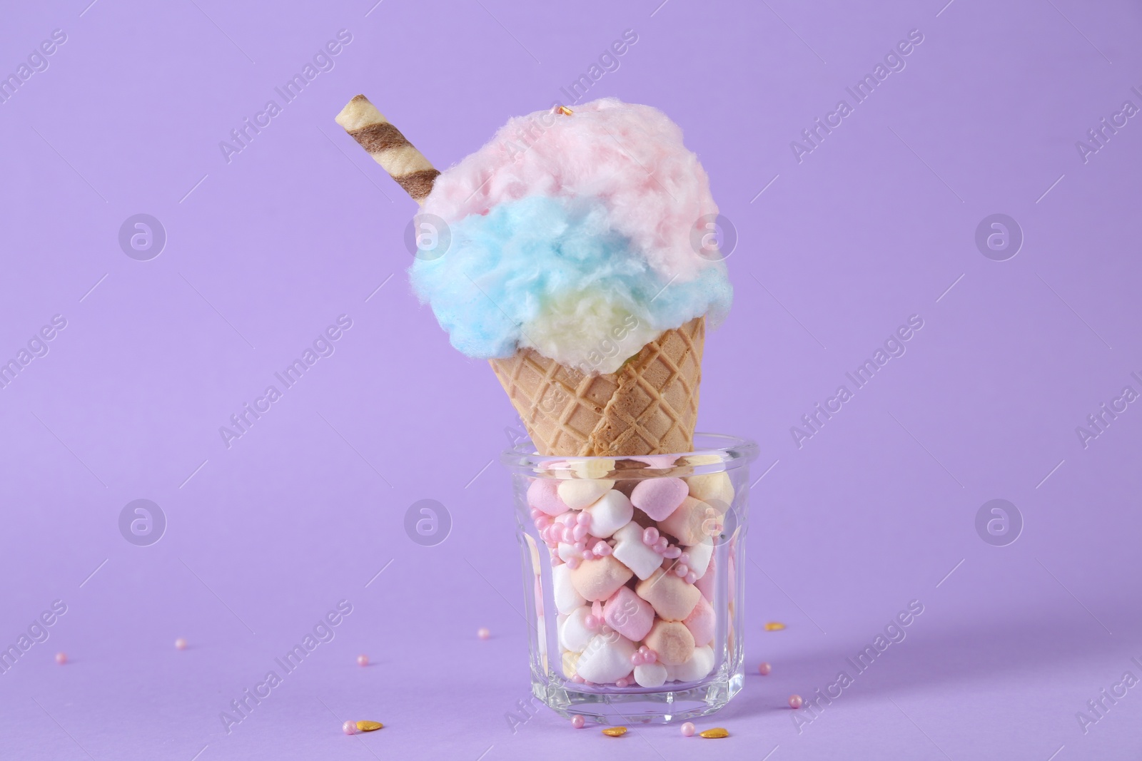 Photo of Sweet cotton candy in waffle cone on purple background, closeup