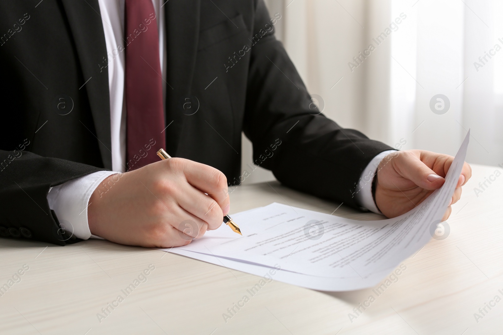 Photo of Notary signing document at wooden table indoors, closeup