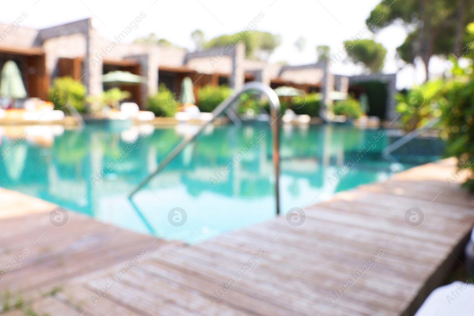 Photo of Outdoor swimming pool with wooden deck, blurred view. Luxury resort
