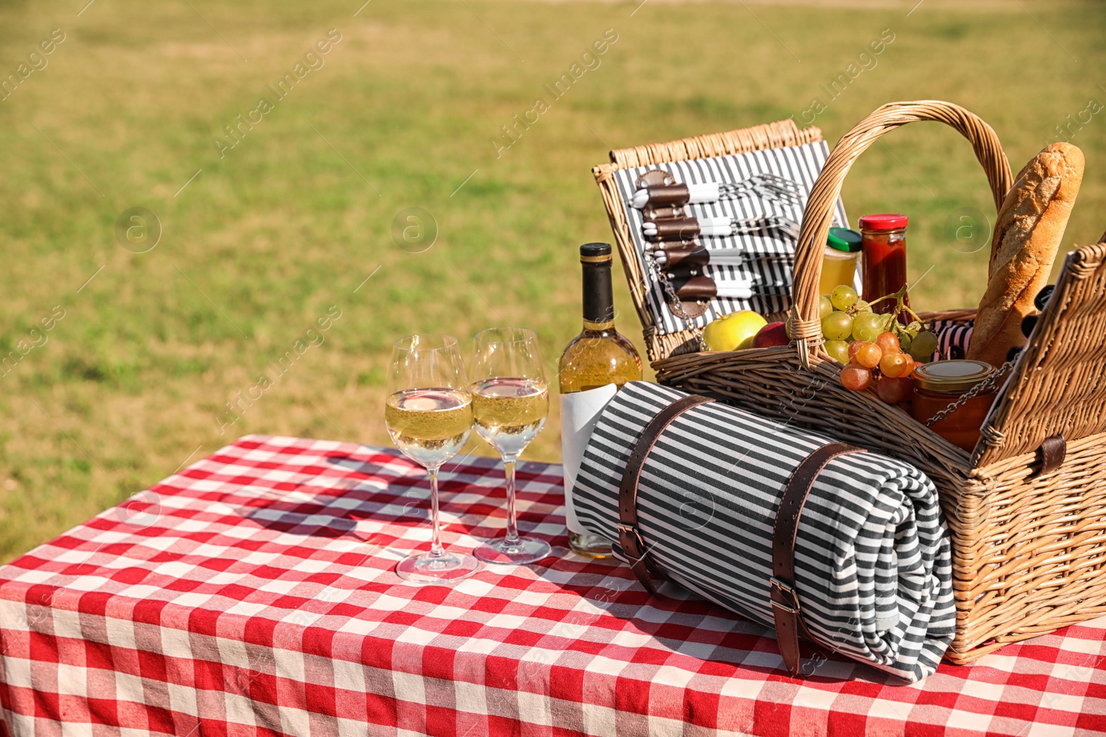 Photo of Picnic basket with wine, snacks and mat on table in park. Space for text