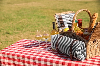 Picnic basket with wine, snacks and mat on table in park. Space for text