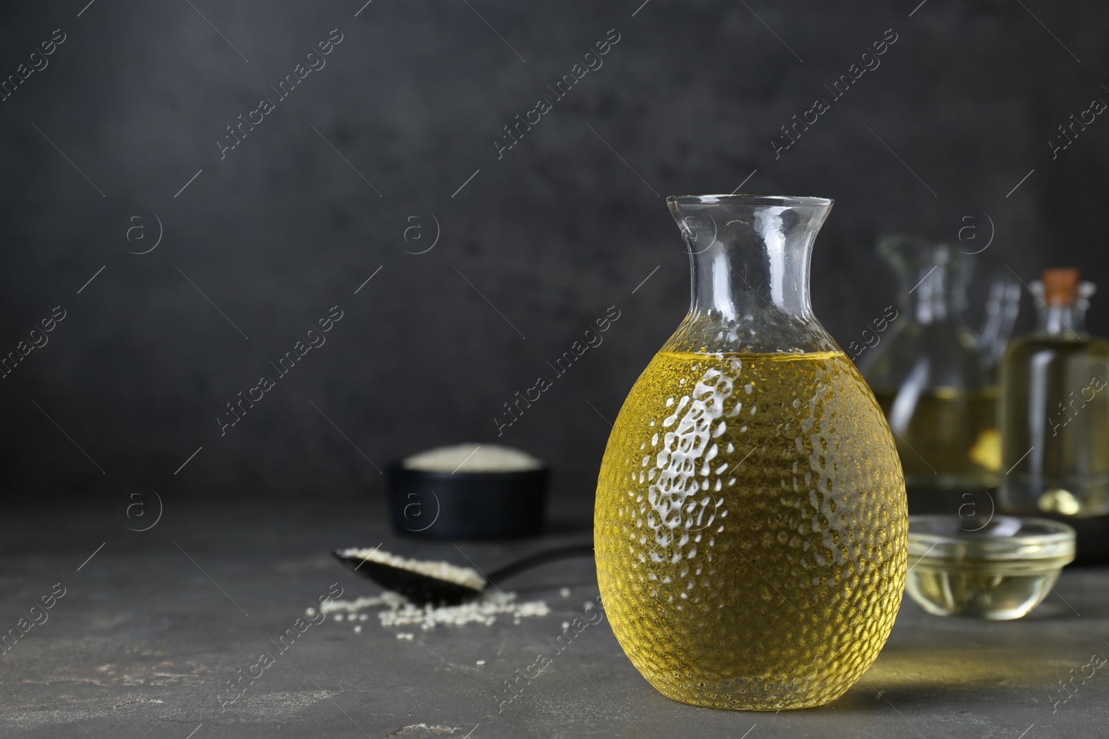 Photo of Fresh sesame oil in glass bottle on grey table. Space for text
