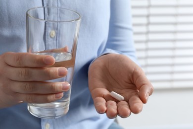 Photo of Woman with glass of water and pill on blurred background, closeup