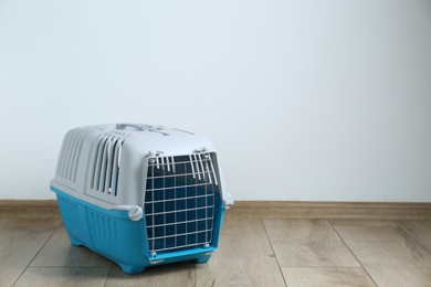 Photo of Light blue pet carrier on floor near white wall. Space for text