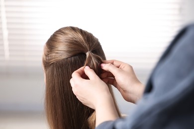 Professional stylist braiding woman's hair indoors, closeup