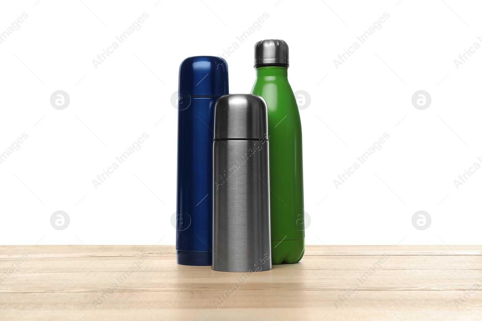 Photo of Stylish thermo bottles on wooden table against white background