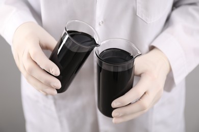 Woman pouring black crude oil into beaker on light background, closeup