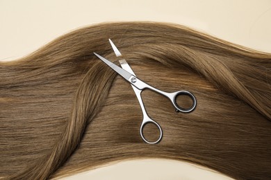 Photo of Professional hairdresser scissors with dark blonde hair on beige background, top view. Haircut tool