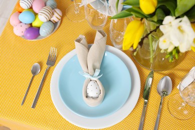 Photo of Festive table setting with painted eggs, plate and vase of tulips, view from above. Easter celebration