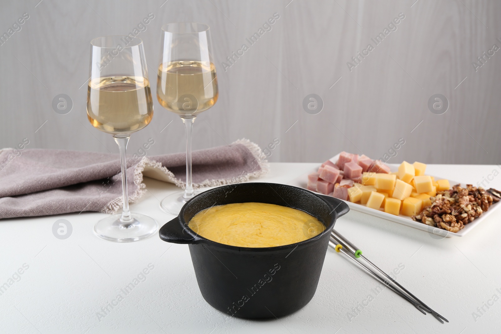 Photo of Fondue with tasty melted cheese, forks, different products and aromatic wine in glasses on white table