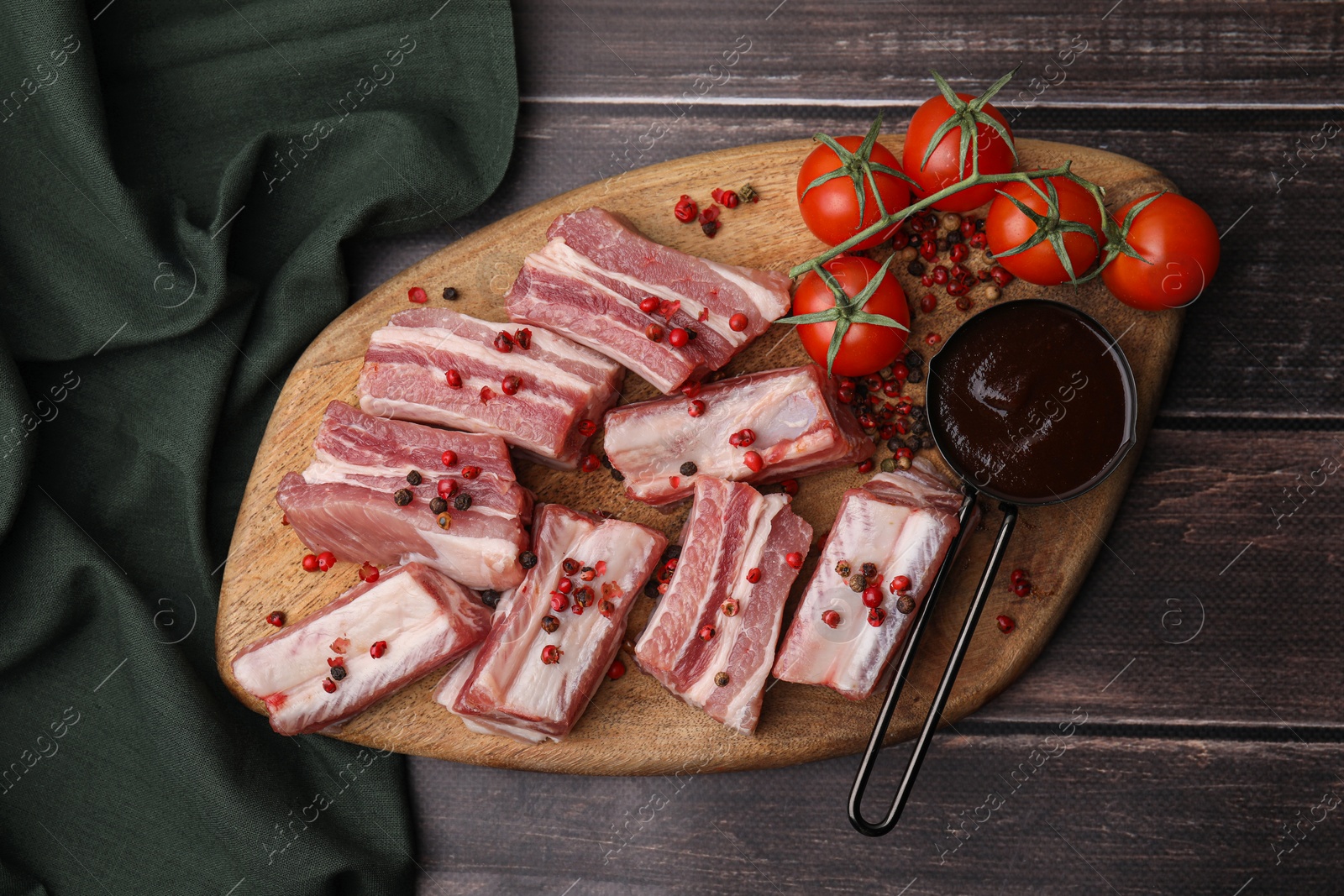 Photo of Cut raw pork ribs with peppercorns, tomatoes and sauce on wooden table, top view