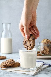 Photo of Woman dipping tasty chocolate chip cookie into glass of milk at white marble table, closeup