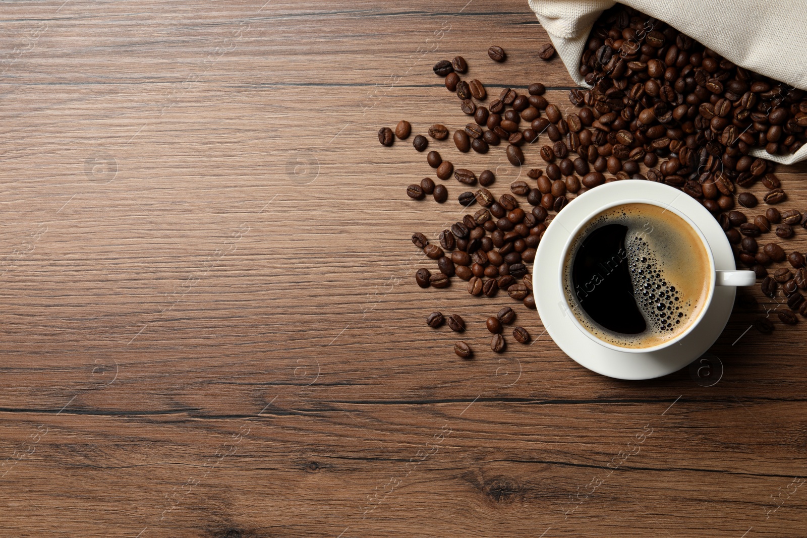 Photo of Cup of aromatic hot coffee and beans on wooden table, flat lay. Space for text