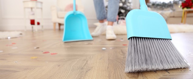 Image of Woman cleaning messy room after New Year party, focus on broom. Banner design