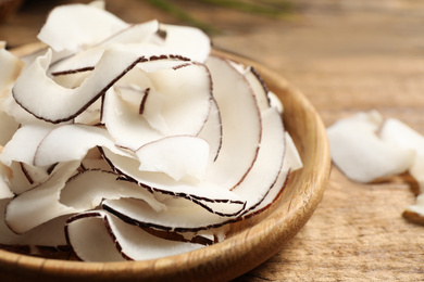 Photo of Tasty coconut chips in wooden plate, closeup