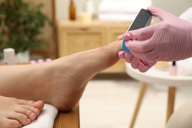 Professional pedicurist filing client`s toenails in beauty salon, closeup