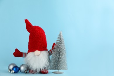 Photo of Cute Christmas gnome, small decorative fir tree and festive balls on light blue background. Space for text