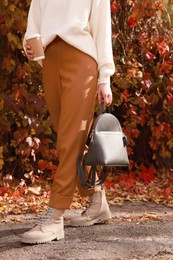 Young woman with stylish grey backpack and hot drink in autumn park, closeup