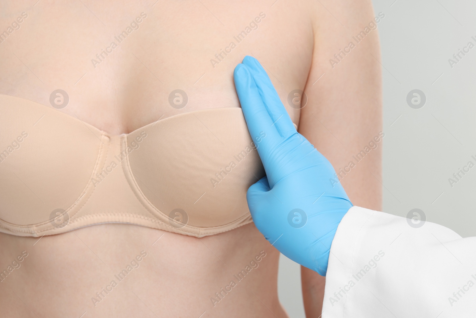 Photo of Mammologist checking woman's breast on light grey background, closeup