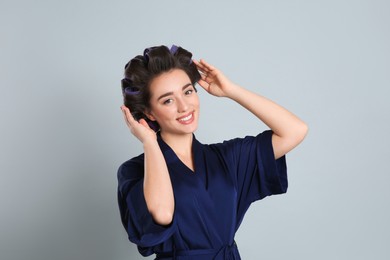 Photo of Happy young woman in silk bathrobe with hair curlers on grey background