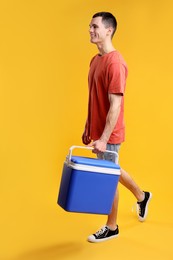 Man with blue cool box walking on orange background