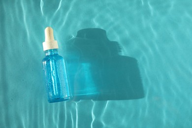 Bottle of cosmetic serum in water on turquoise background, top view. Space for text