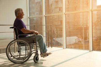 Senior man sitting in wheelchair near window at home