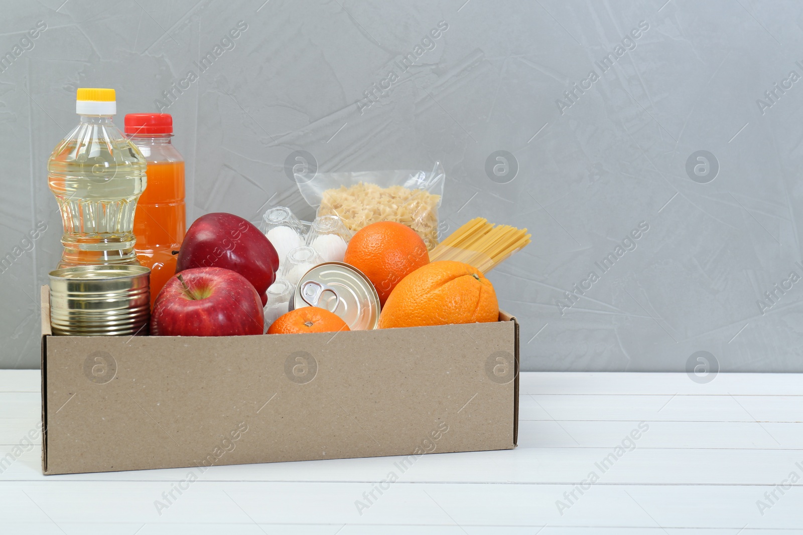 Photo of Humanitarian aid. Different food products for donation in box on white wooden table. Space for text