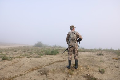Photo of Man wearing camouflage with hunting rifle outdoors, back view. Space for text