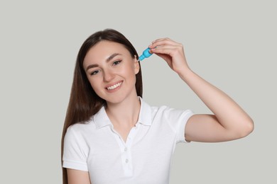 Young woman using ear drops on light grey background