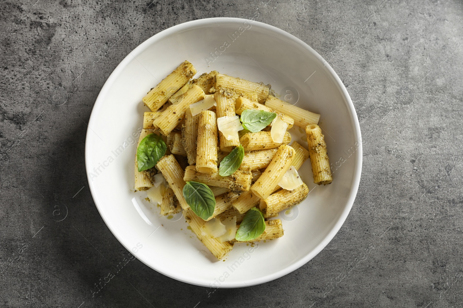 Photo of Plate with delicious basil pesto pasta on gray table, top view