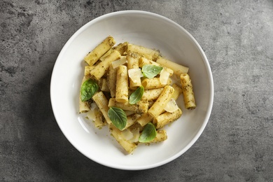 Plate with delicious basil pesto pasta on gray table, top view