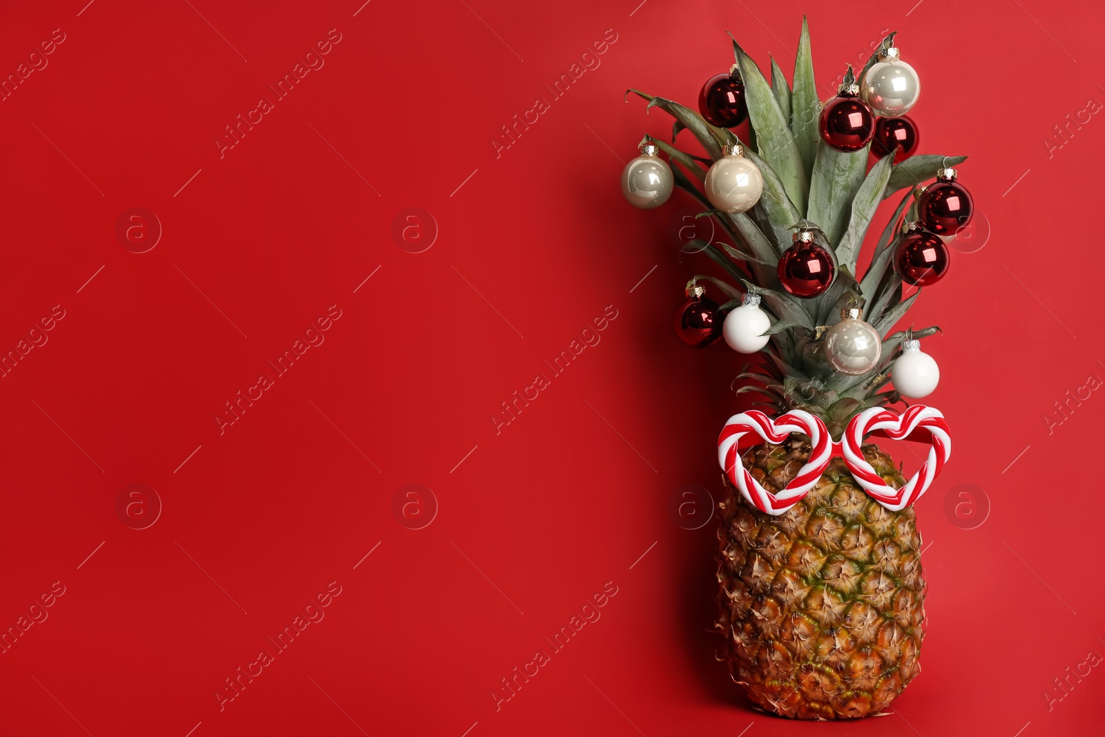 Photo of Pineapple with party glasses and Christmas tree balls on red background, space for text. Creative concept