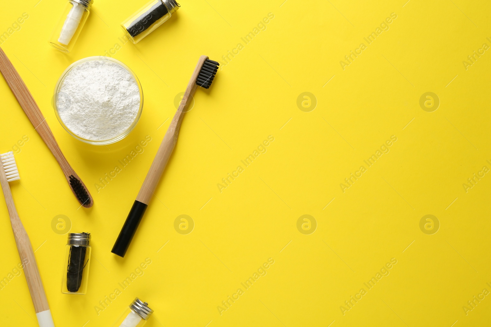 Photo of Bowl of tooth powder, brushes and dental flosses on yellow background, flat lay. Space for text