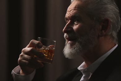 Senior man in suit drinking whiskey on brown background