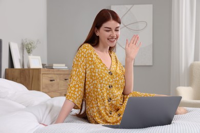 Happy woman having video chat via laptop on bed in bedroom