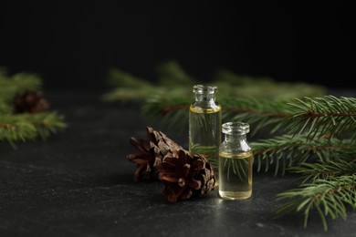 Photo of Pine essential oil, cones and branches on black table. Space for text
